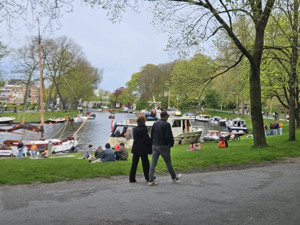Park en kanaal met boten en passanten.