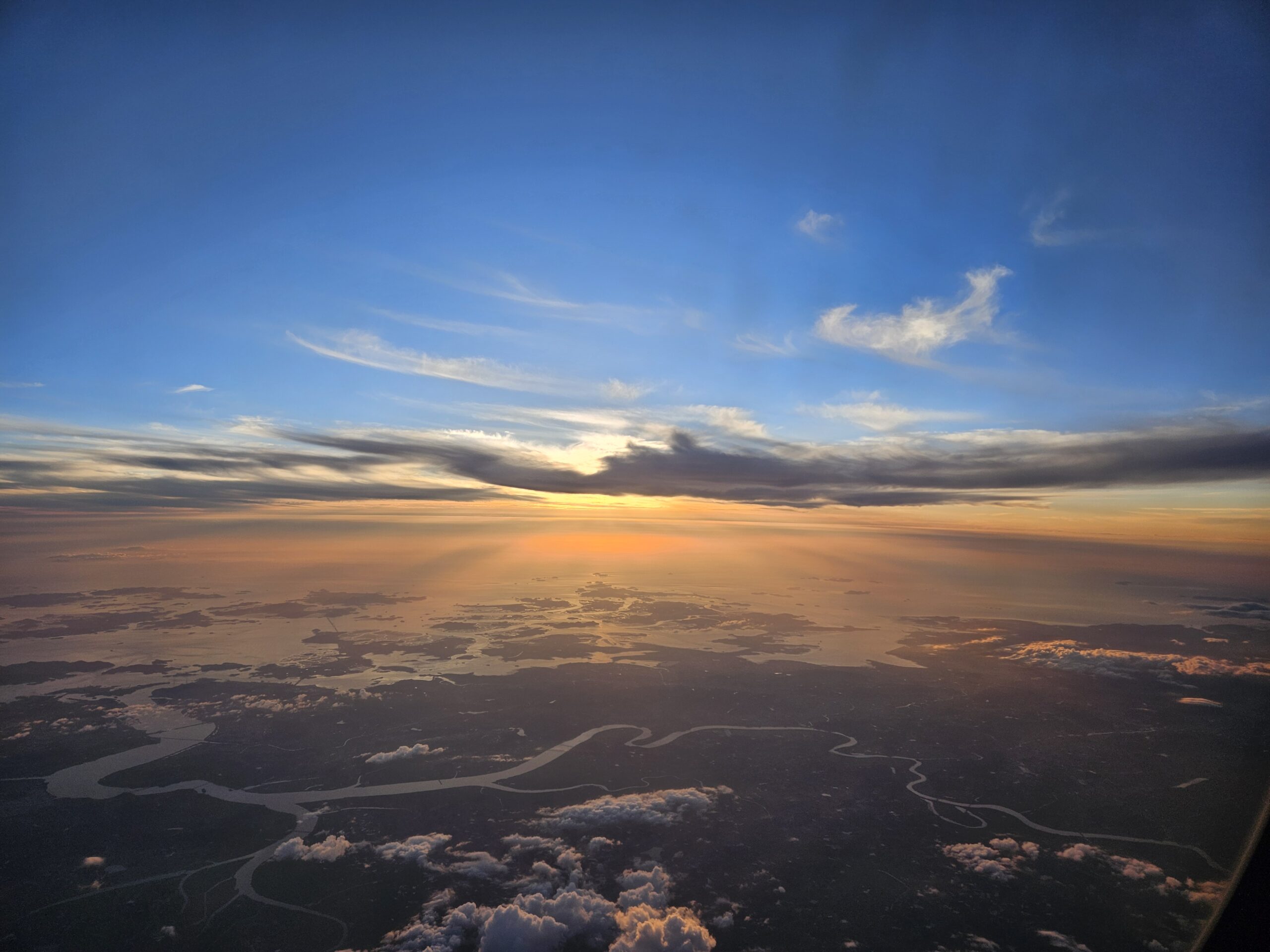 Zonsondergang boven een landschap met rivieren en wolken, gezien vanuit een vliegtuigraam.