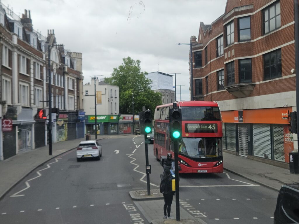 Rode dubbeldekkerbus rijdt door een straat in Zuid-Londen, gezien vanaf de bovenverdieping van een andere bus.