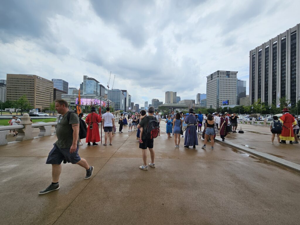 Bezoekers wandelen over het natte Gwanghwamun Square in Seoul terwijl donkere regenwolken boven de stad hangen.
