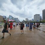 Bezoekers wandelen over het natte Gwanghwamun Square in Seoul terwijl donkere regenwolken boven de stad hangen.