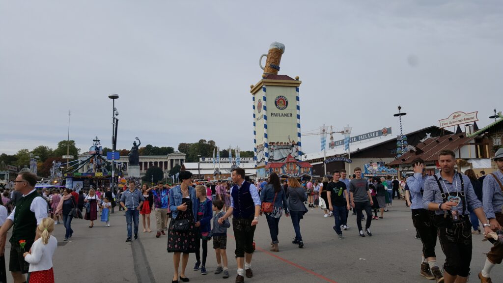 oktoberfest-munchen.jpg Bezoekers wandelen over de Theresienwiese tijdens het Oktoberfest in München, met de iconische Paulaner-toren op de achtergrond.
