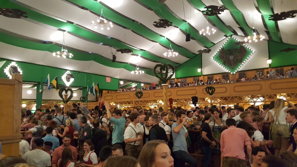 Een volle feesttent tijdens het Oktoberfest waar bezoekers samen zingen, dansen en proosten. Groses Kino.