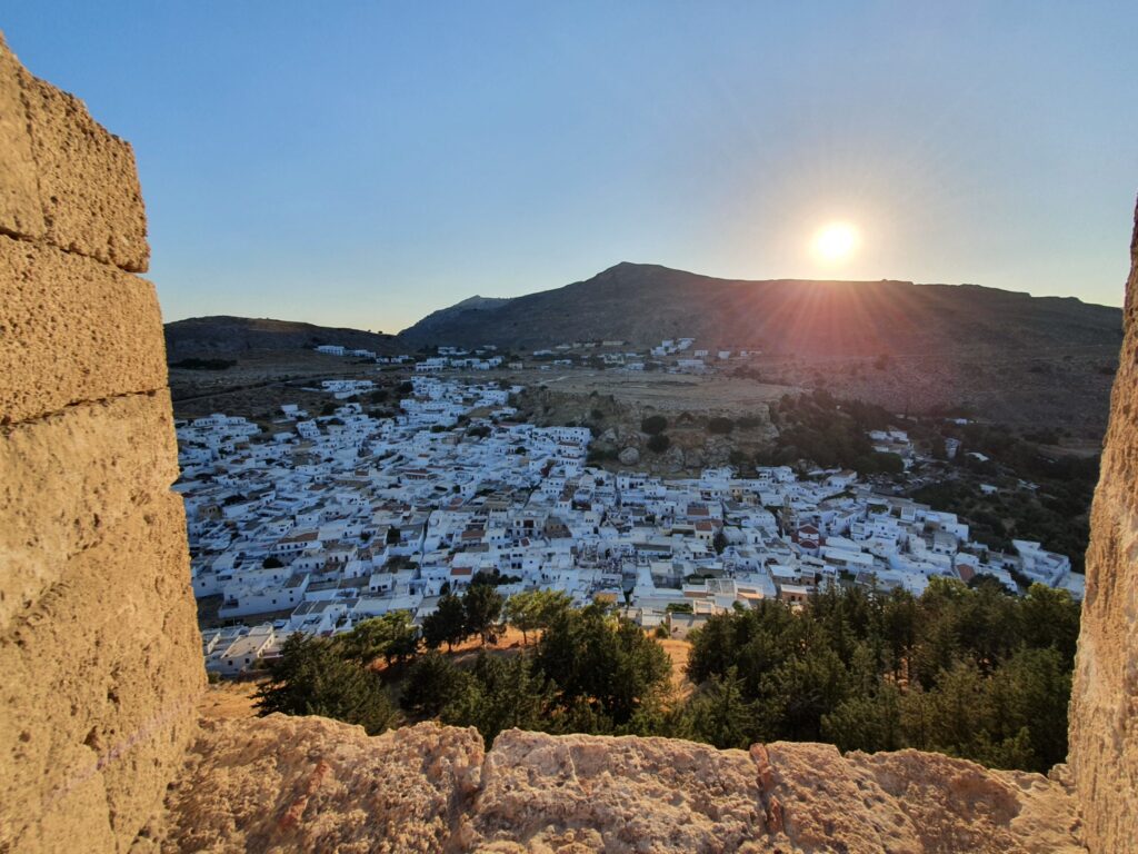 Witte huizen van Lindos tussen stenen muren, met de laagstaande zon boven de heuvels.